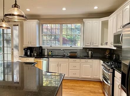White kitchen with granite countertops, stainless steel appliances, and large windows.