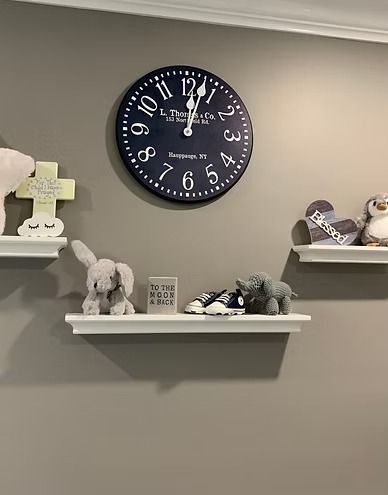 A dark blue clock hangs above two shelves with stuffed animals and decorations on a gray wall.