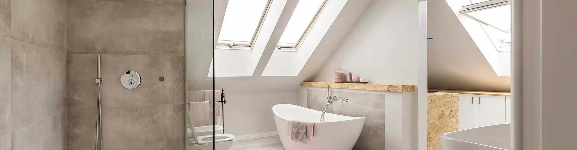 Bathroom with slanted ceiling and skylights, a white freestanding tub, and a shower with gray tile.