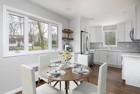 Dining area with round table, four white chairs, and a kitchen with white cabinets.