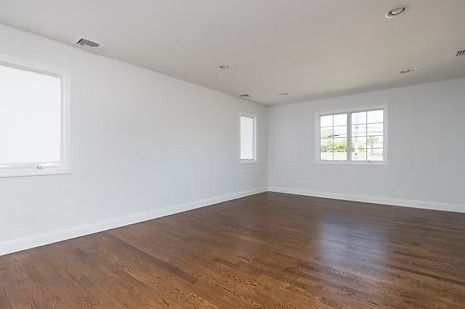 Empty room with wood floor, white walls, and three windows.
