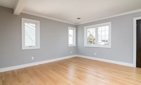 Empty room with wood floors, gray walls, white trim, and windows.