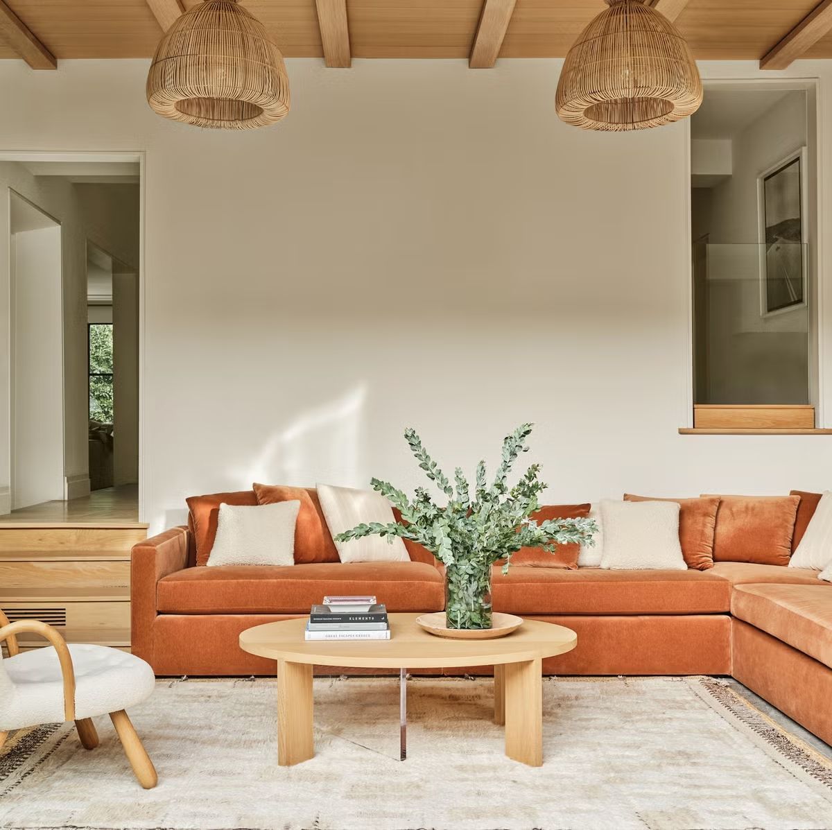 Living room with orange sectional sofa, wood coffee table, and woven pendant lights.
