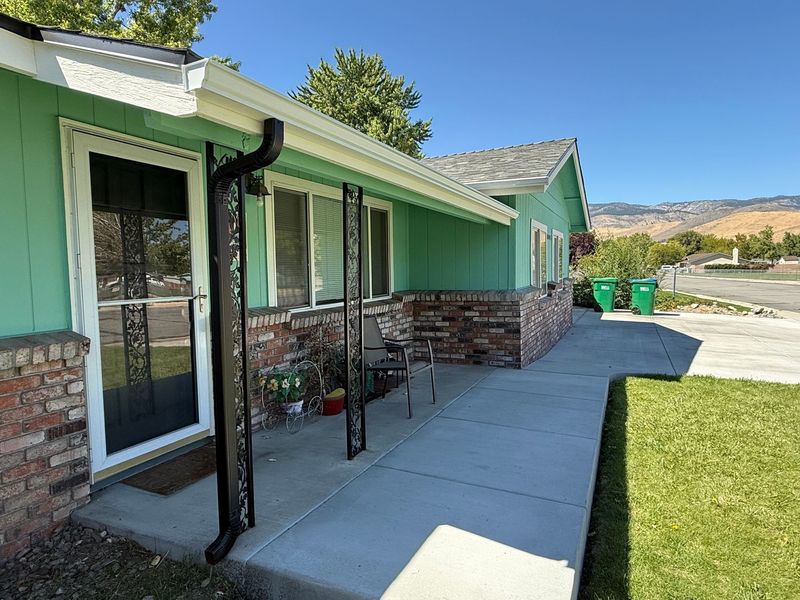 Green house with brick accents, porch, and a lawn. Two green trash cans are nearby.