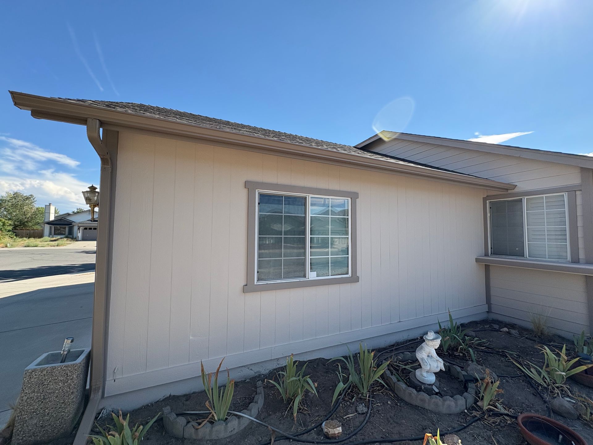 Beige house exterior with a window, roof overhang, and small garden on a sunny day.
