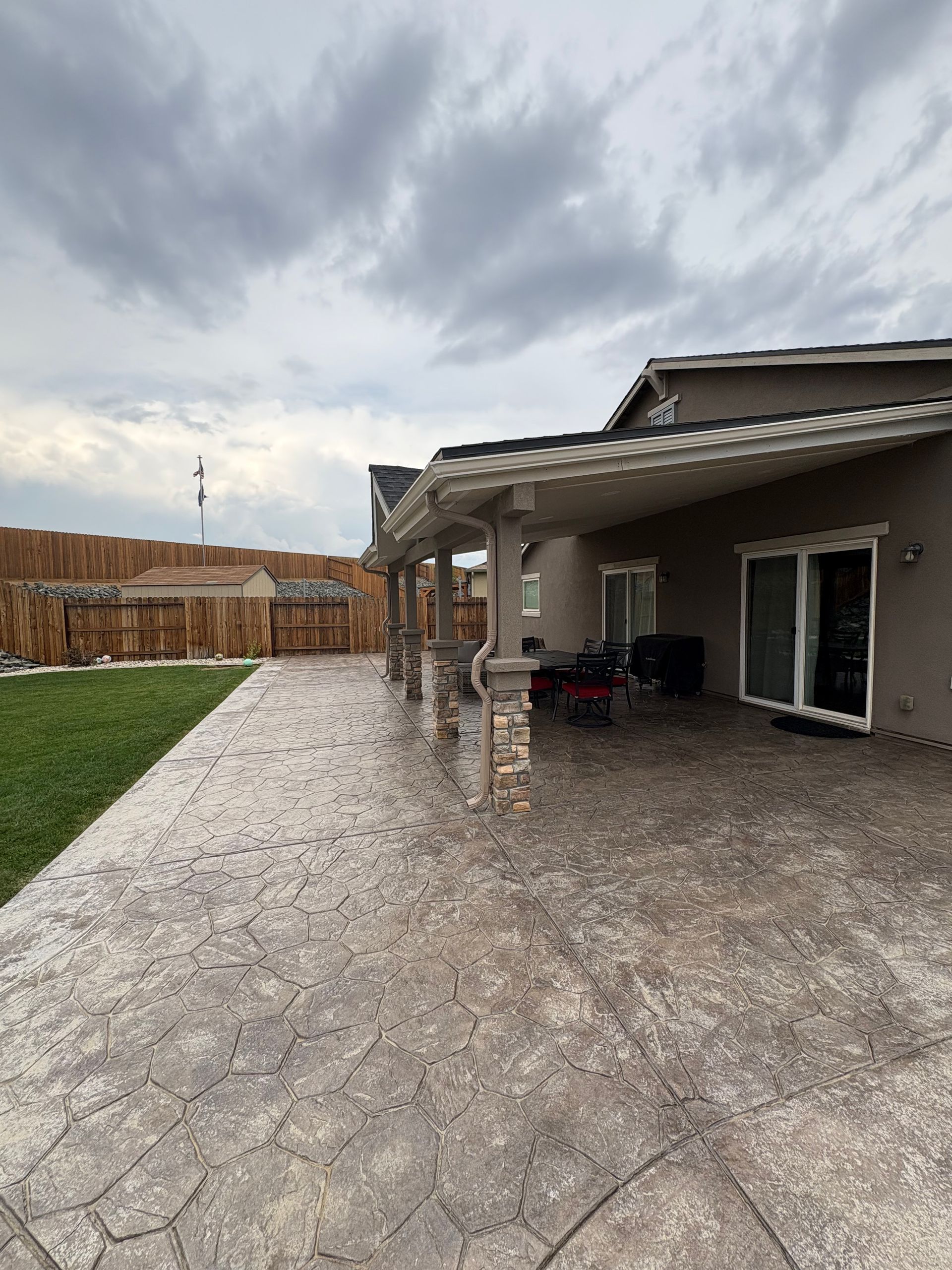 Covered patio with textured concrete floor, overlooking a lawn. Overcast sky.