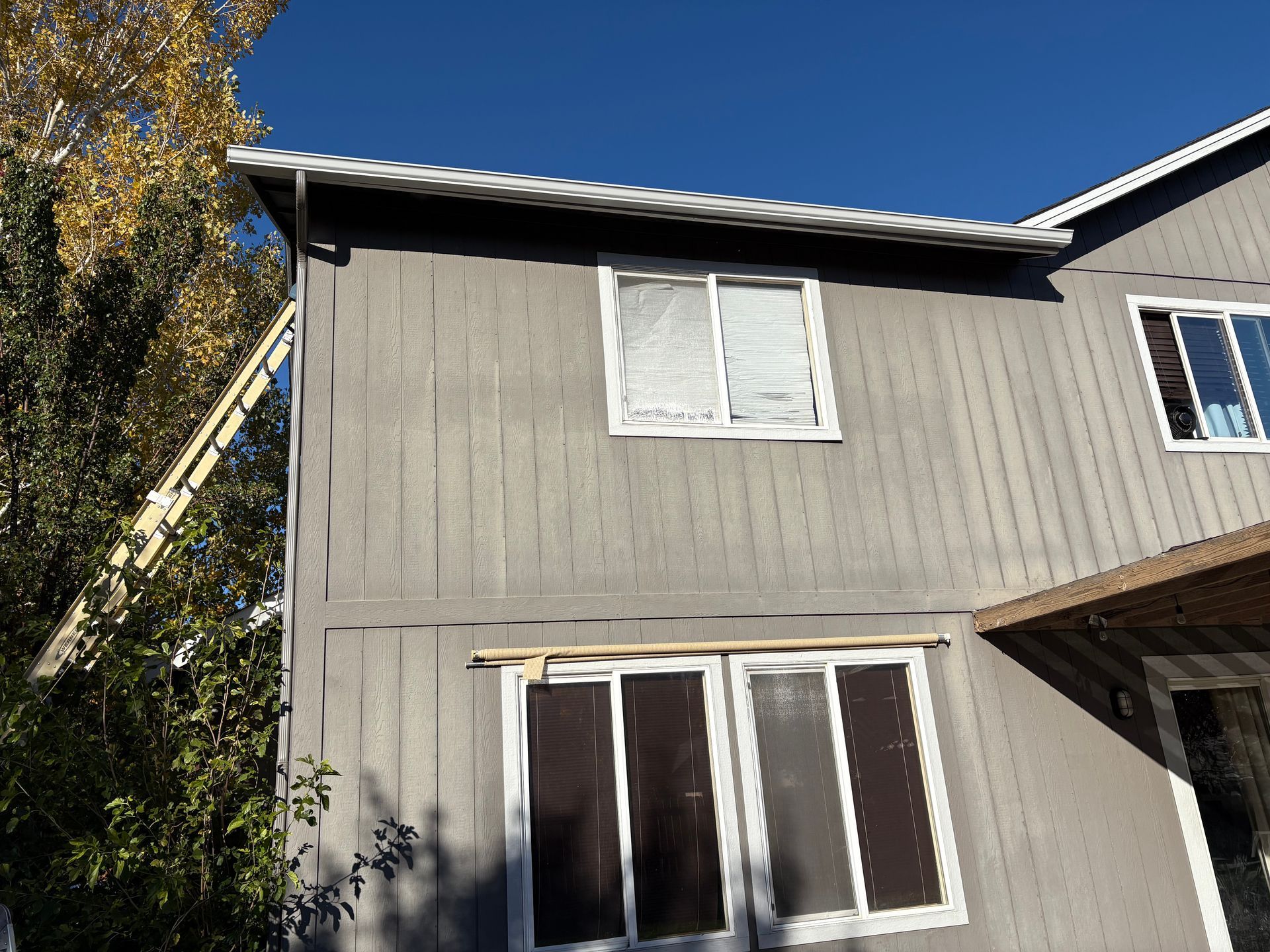 Gray two-story house with white-framed windows under a clear blue sky.