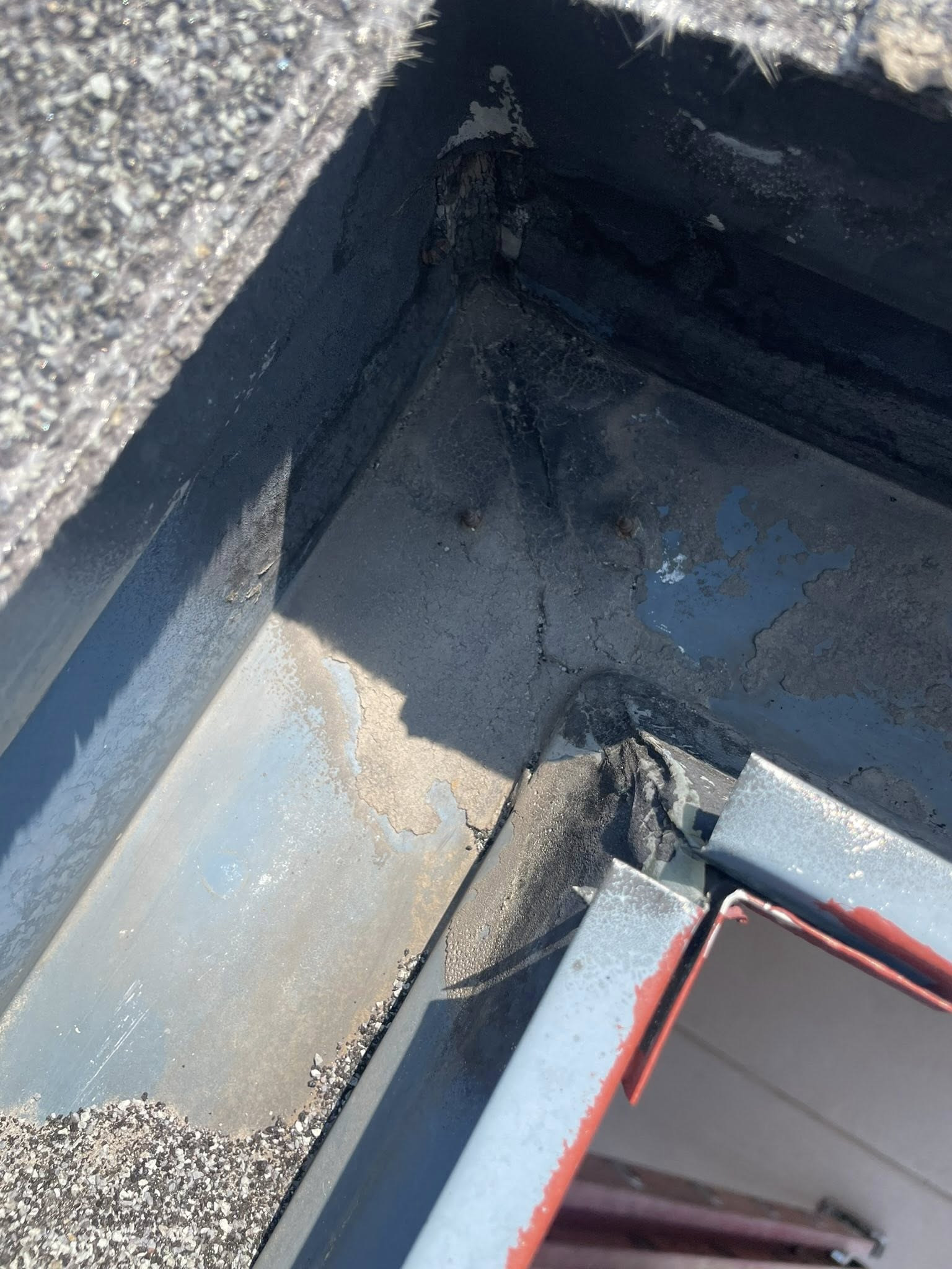 Overhead view of a roof corner with black sealant and metal flashing, showing wear and potential leaks.