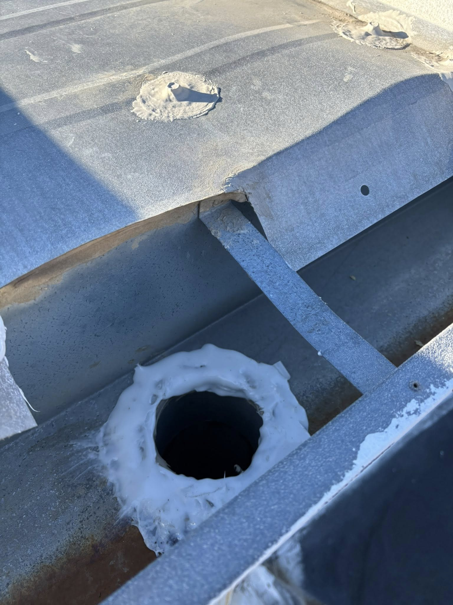 Metal roof drain surrounded by white sealant.