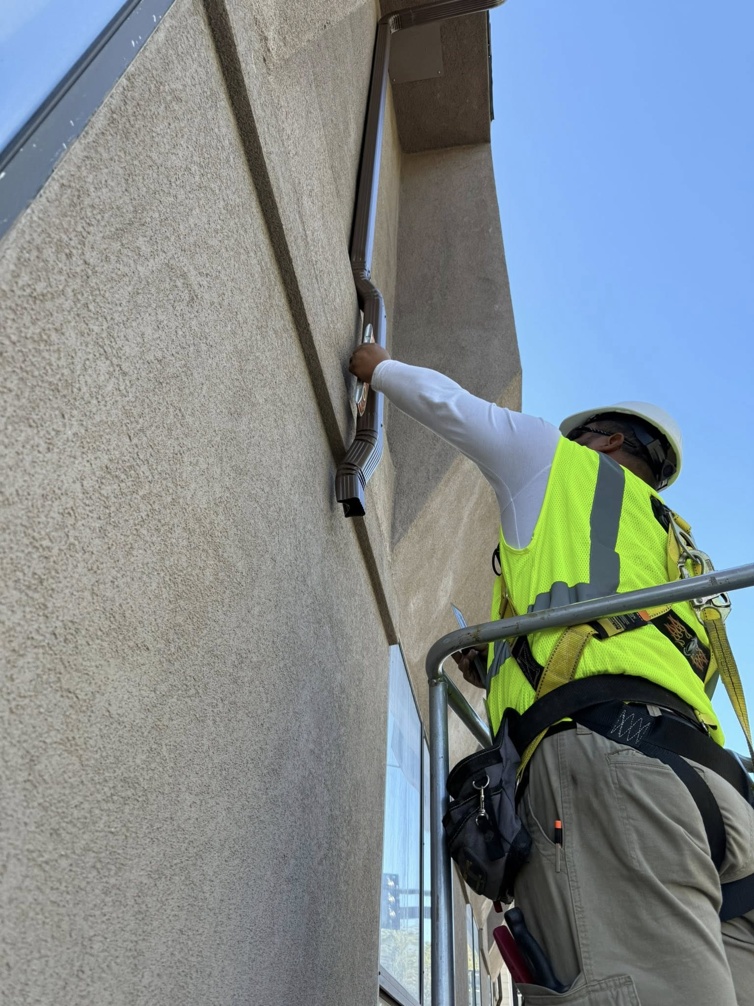 Worker in safety vest on lift, reaching towards a window on a stucco building.