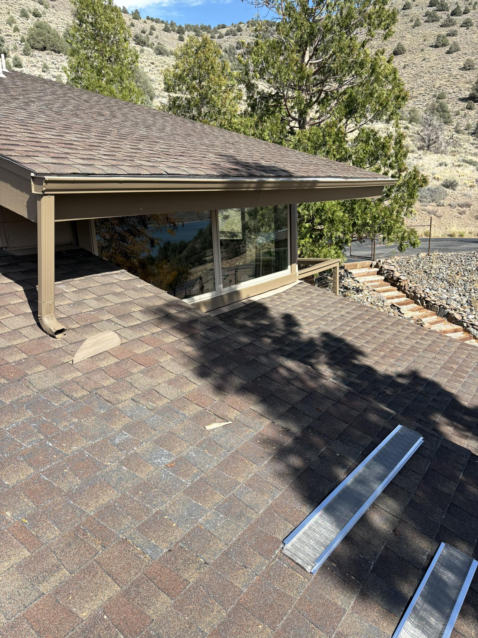 A house with a shingle roof and glass windows. Two metal ramps on a brick patio.