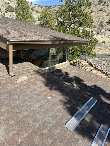 A house with a shingle roof and glass windows. Two metal ramps on a brick patio.