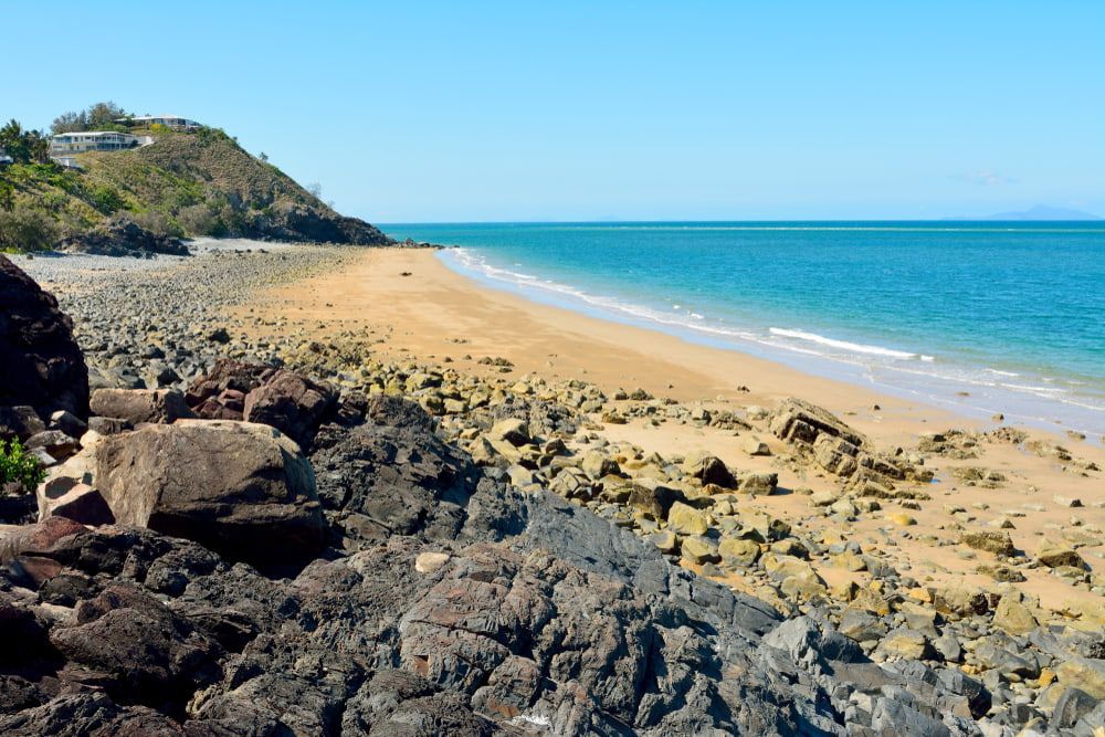 A Rocky Beach with A Large Rock in The Foreground and A Large Body of Water in The Background — Iconic Construction Industries in Mackay, QLD