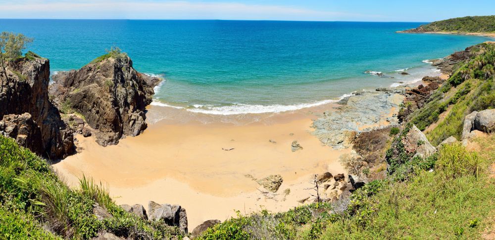 Sandy Beach Surrounded by Rocky Cliffs and Green Vegetation — Iconic Construction Industries in Rockhampton, QLD