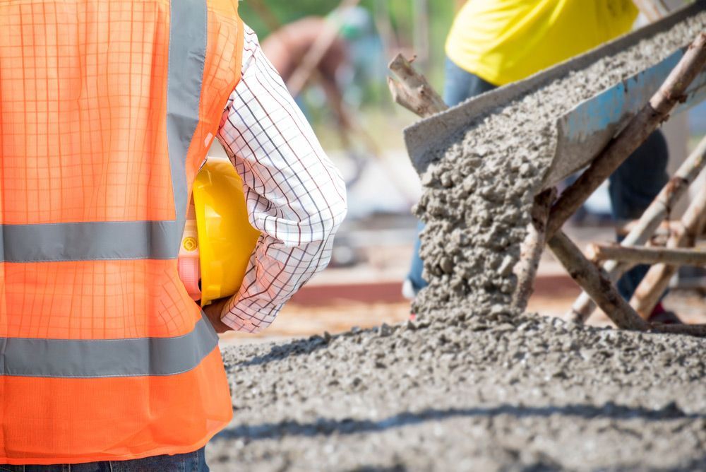 A Construction Worker Wearing a Hard Hat Is Standing in Front of A Wheelbarrow Filled with Concrete — Iconic Construction Industries in Garbutt, QLD