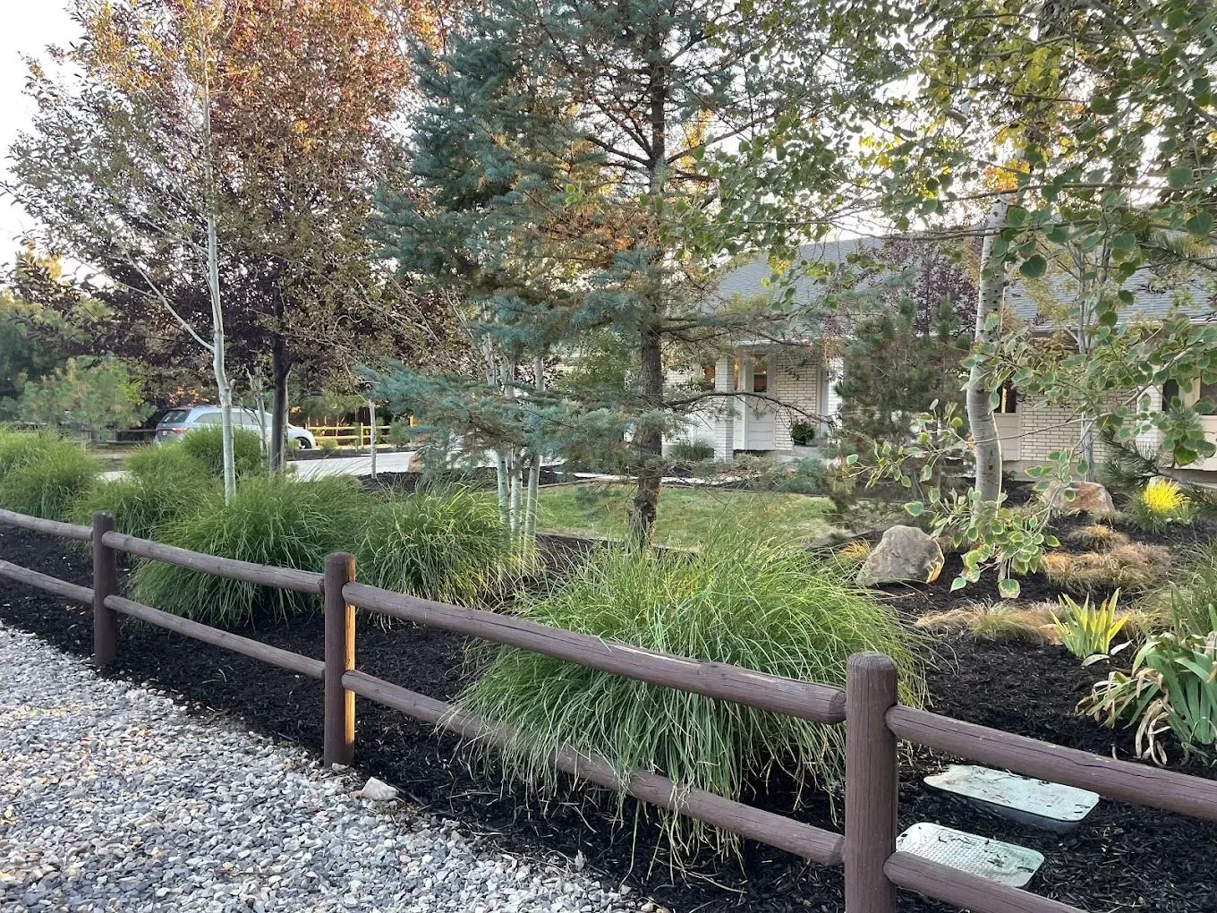 A wooden fence surrounds a lush green garden in front of a house.