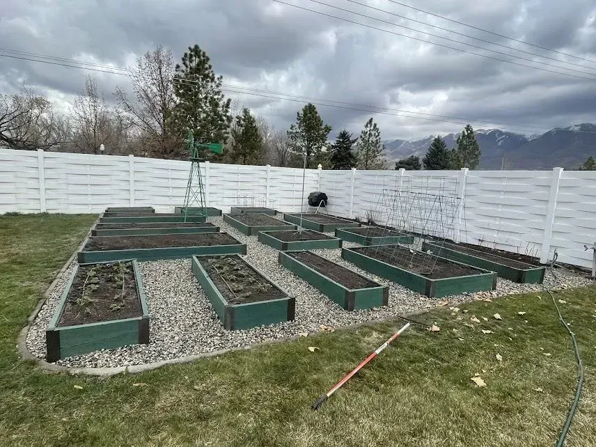 A row of raised garden beds in a backyard with a white fence.