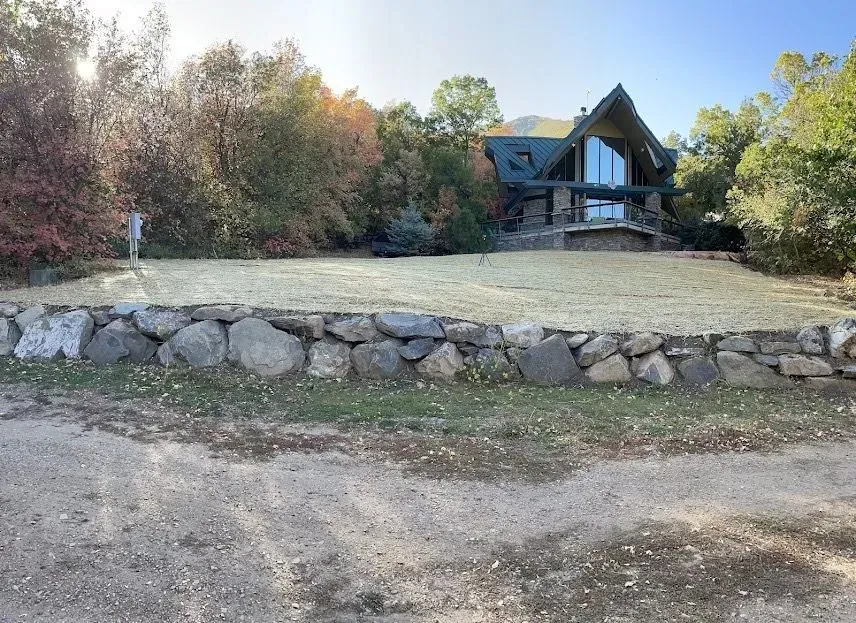 A large house is surrounded by trees and a stone wall.