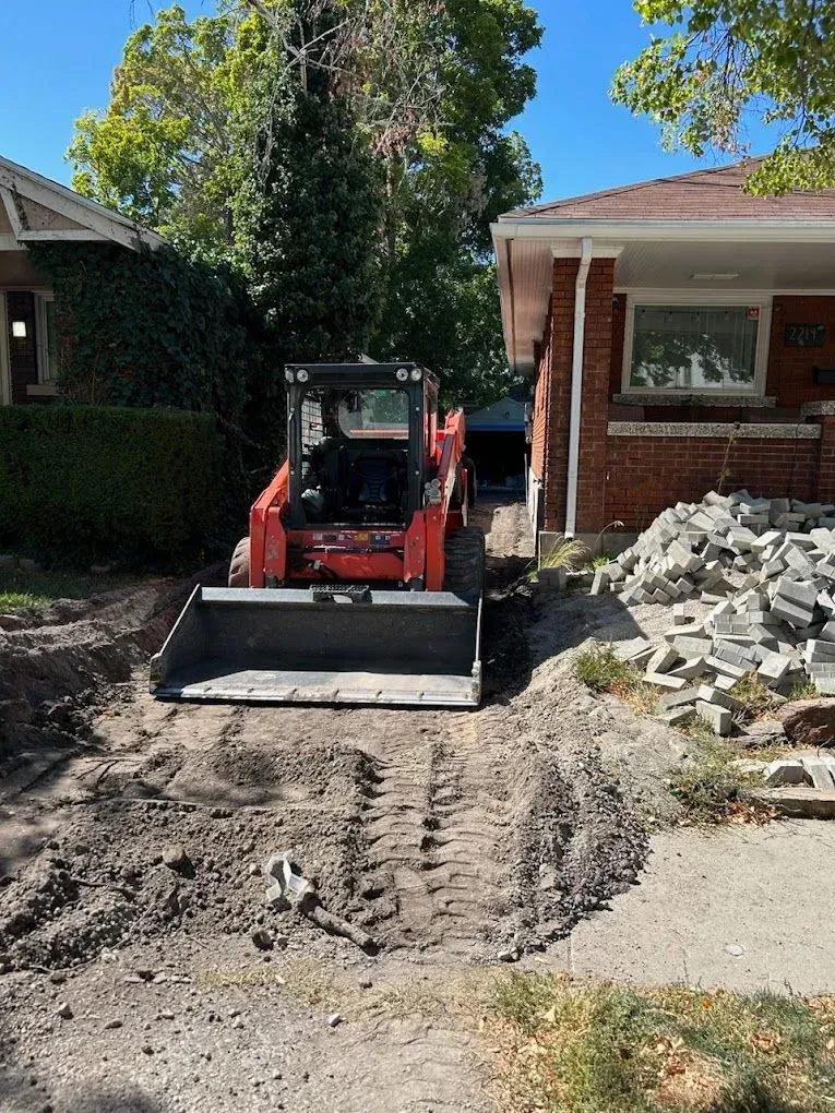 A bulldozer is driving down a dirt road in front of a brick house.