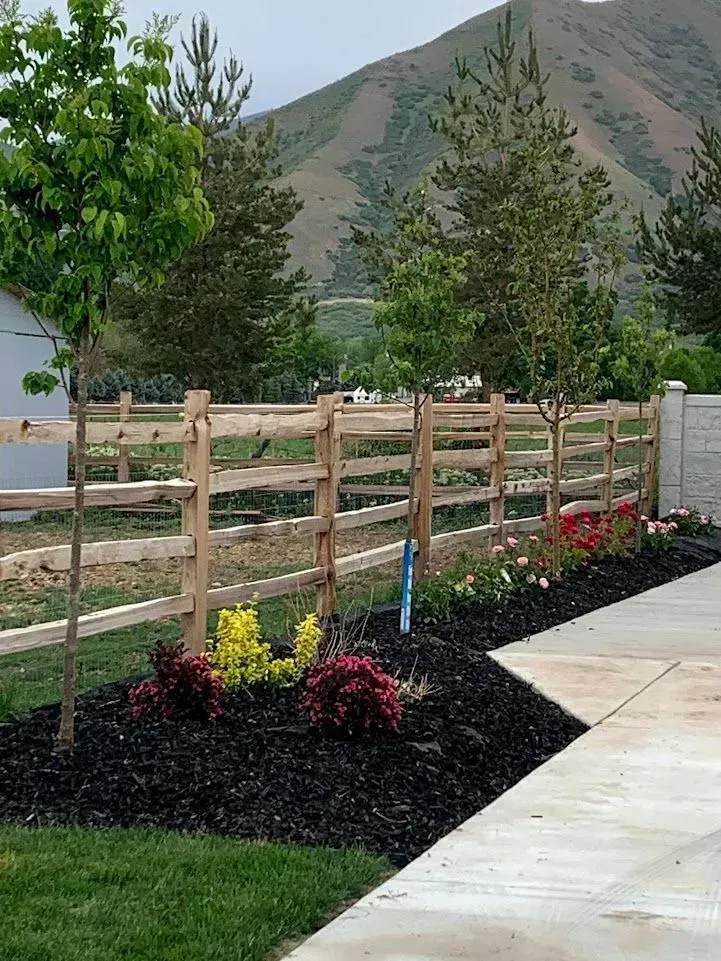 A wooden fence surrounds a lush green yard with mountains in the background.
