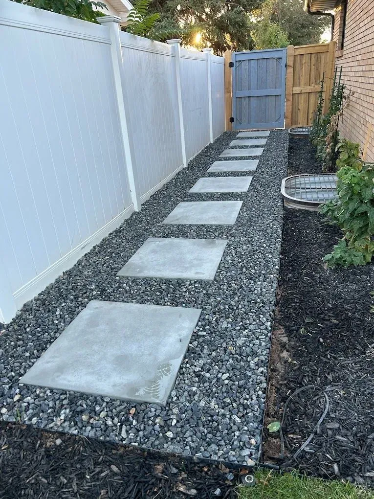 A walkway with concrete stepping stones and gravel next to a fence.