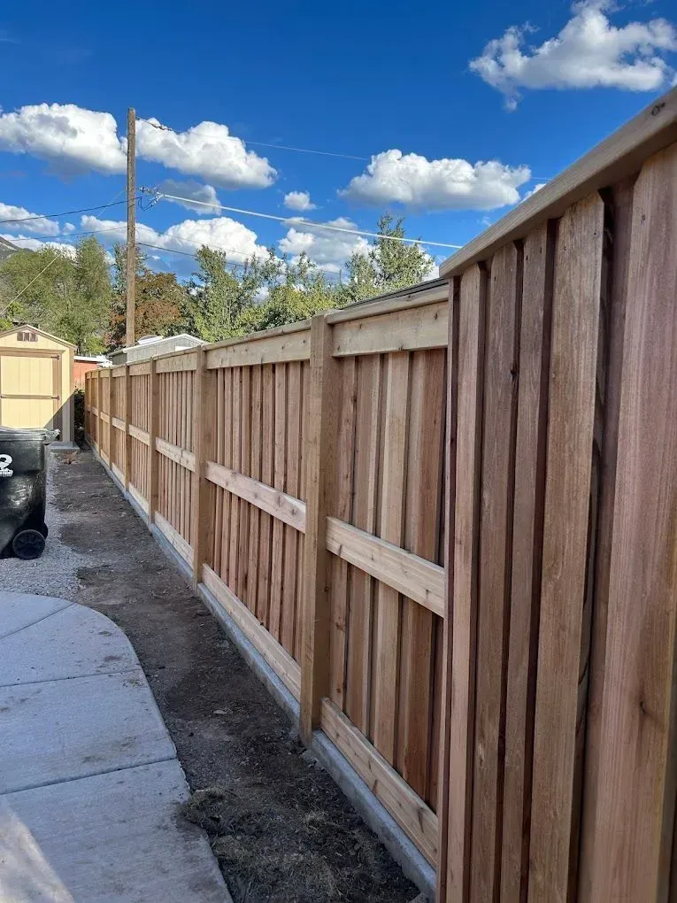 A wooden fence along a sidewalk with a blue sky in the background.