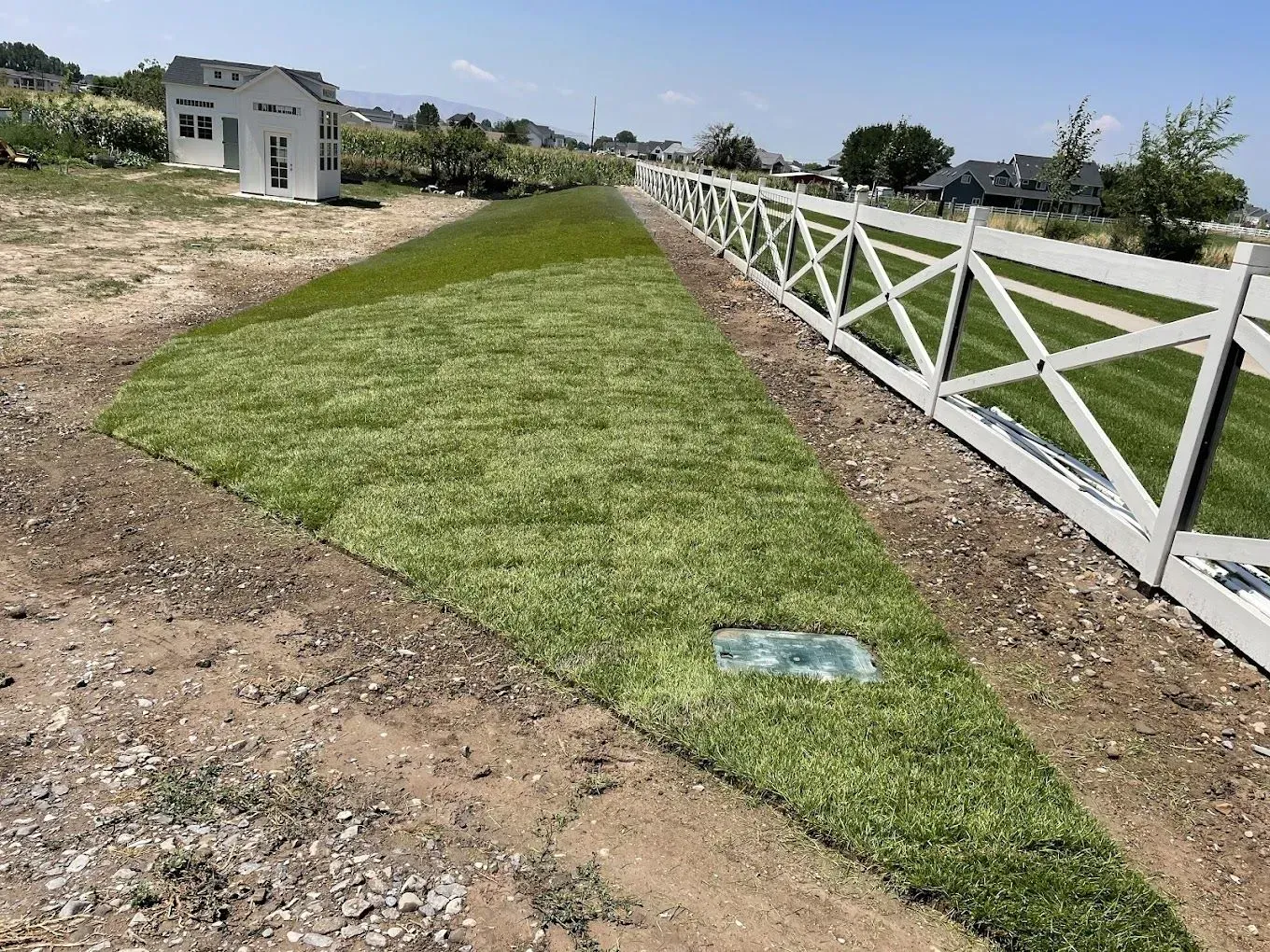 A white fence surrounds a lush green field of grass.