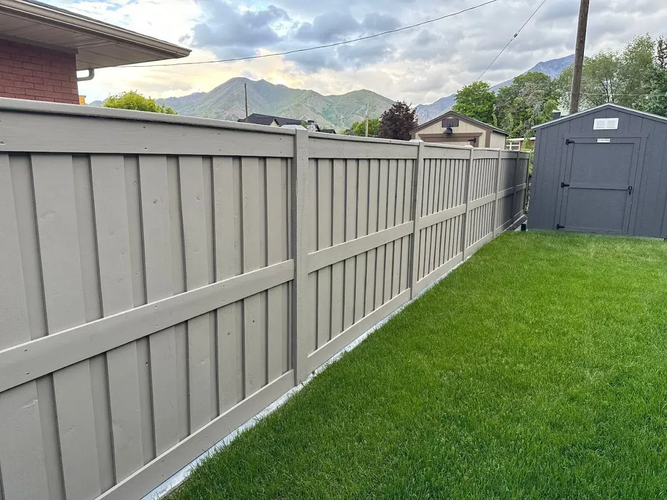 There is a fence in the backyard with a shed in the background.