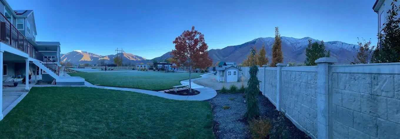 A panoramic view of a backyard with a fence and mountains in the background.