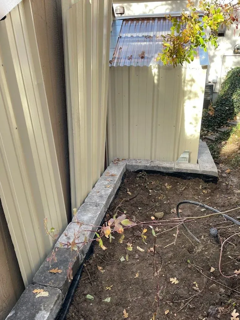 A corner of a house with a fence and a concrete border.
