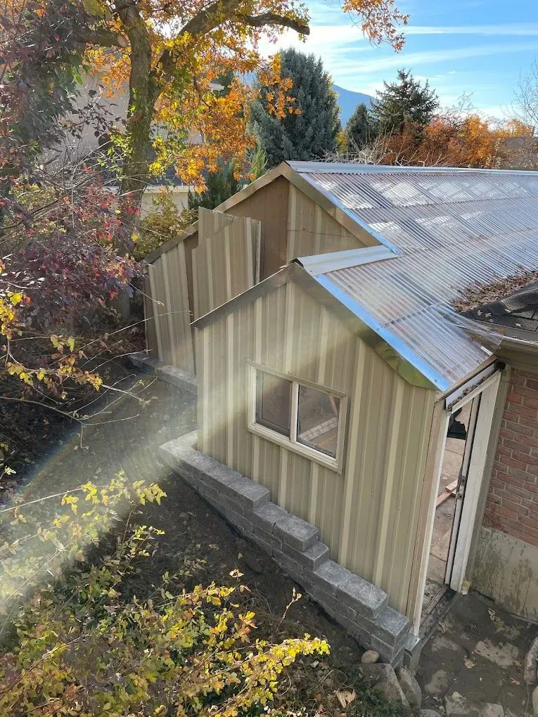 A wooden shed with a metal roof is being built next to a house.
