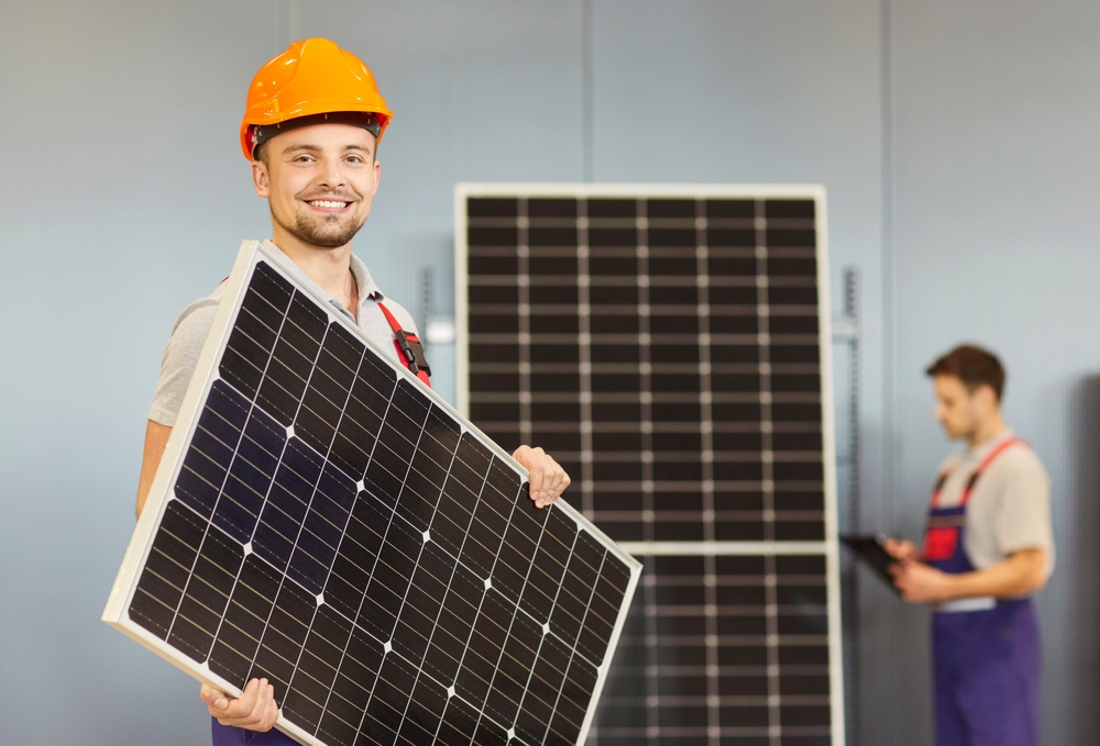 A man in a hard hat is holding a solar panel in his hands.