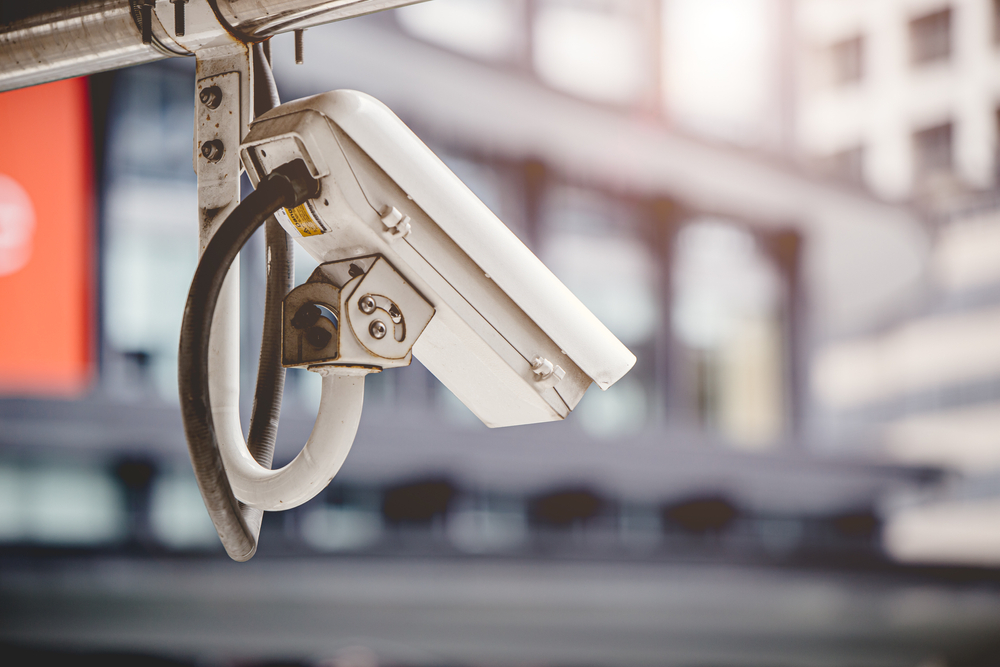 A security camera is hanging from the side of a building.