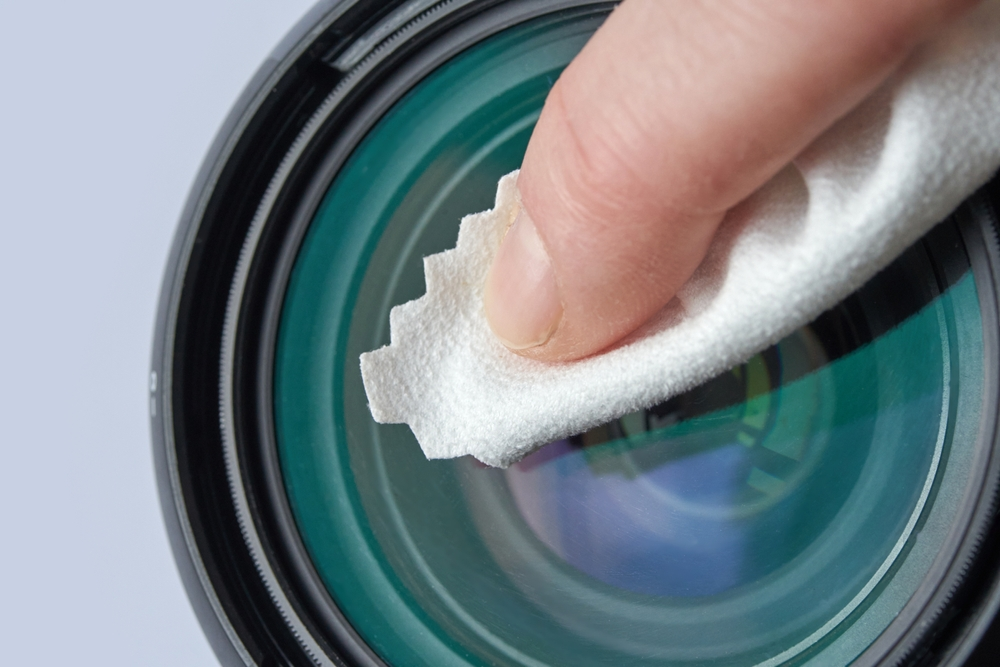 A person is cleaning a camera lens with a cloth.