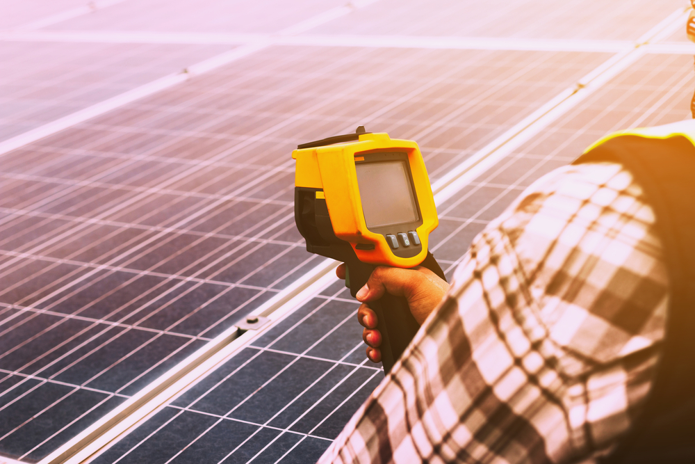 A man is holding a thermometer in front of a solar panel.