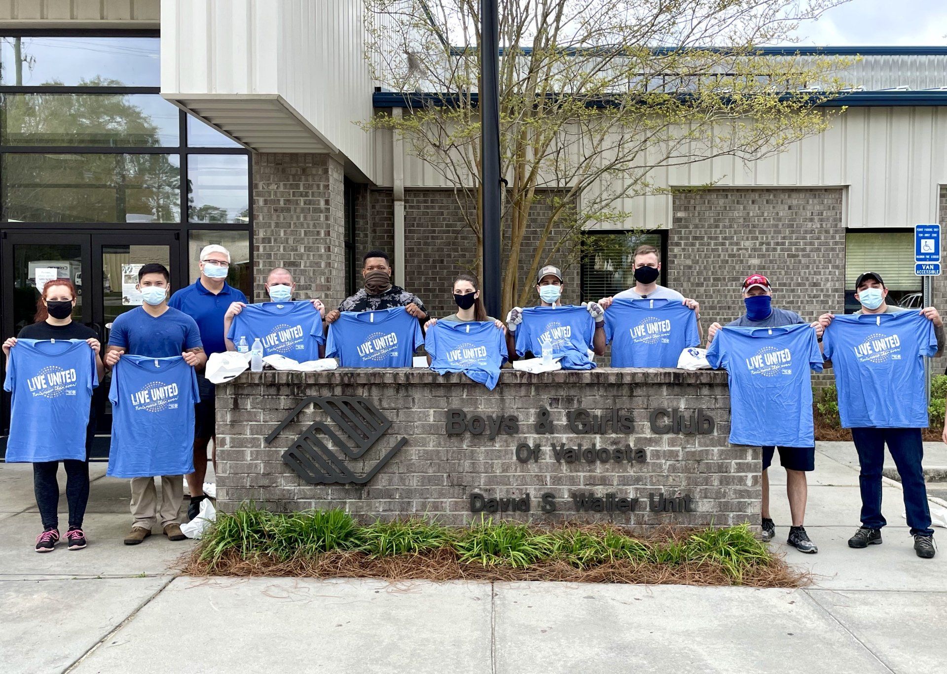 A group of adults outside holding up matching blue shirts posing in front of Boys & Girls Club of Valdosta