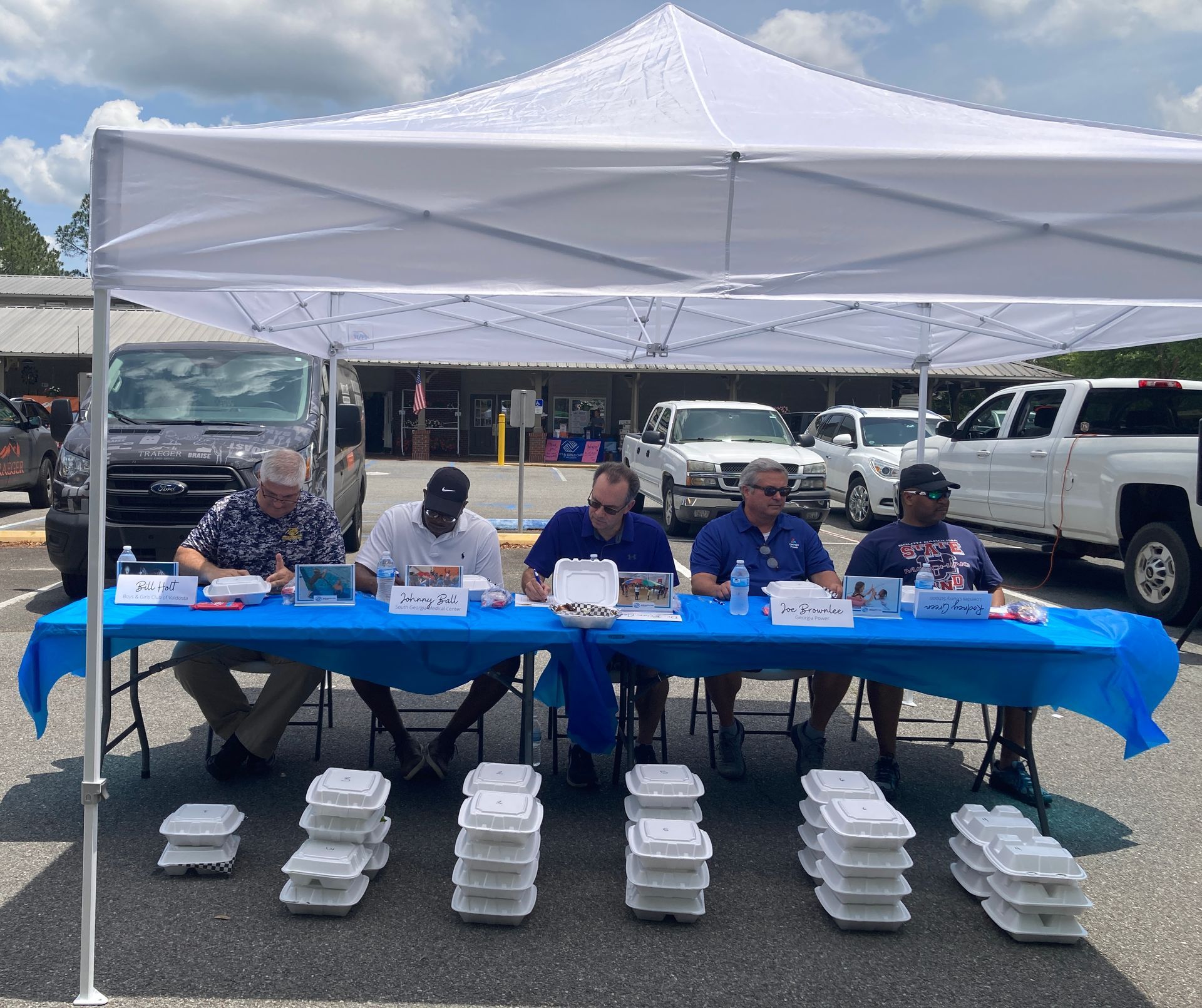 Five people seated at a table under a tent, judging BBQ for BBQ cook-off.