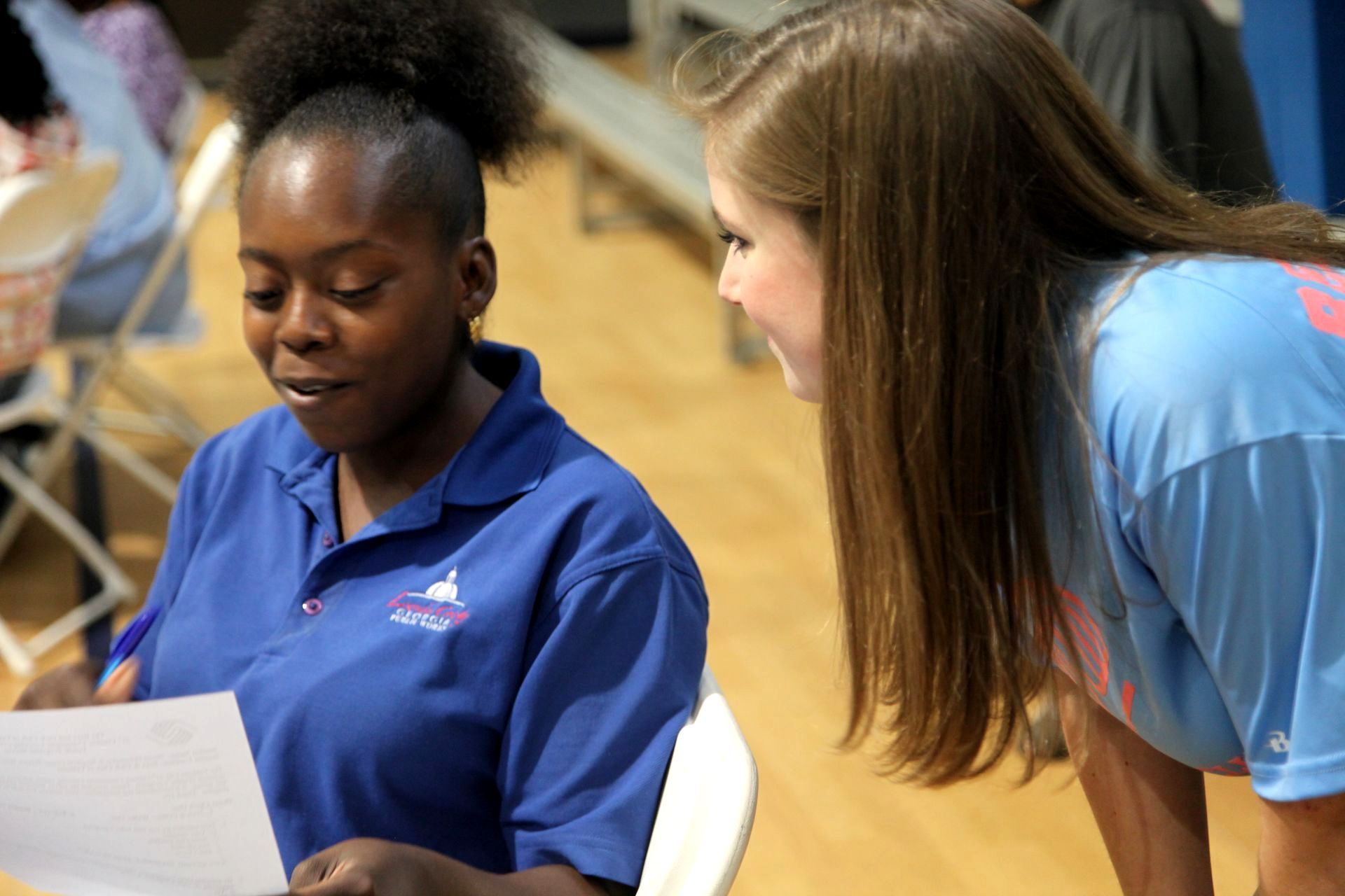 Two young women look at paperwork in a gym.