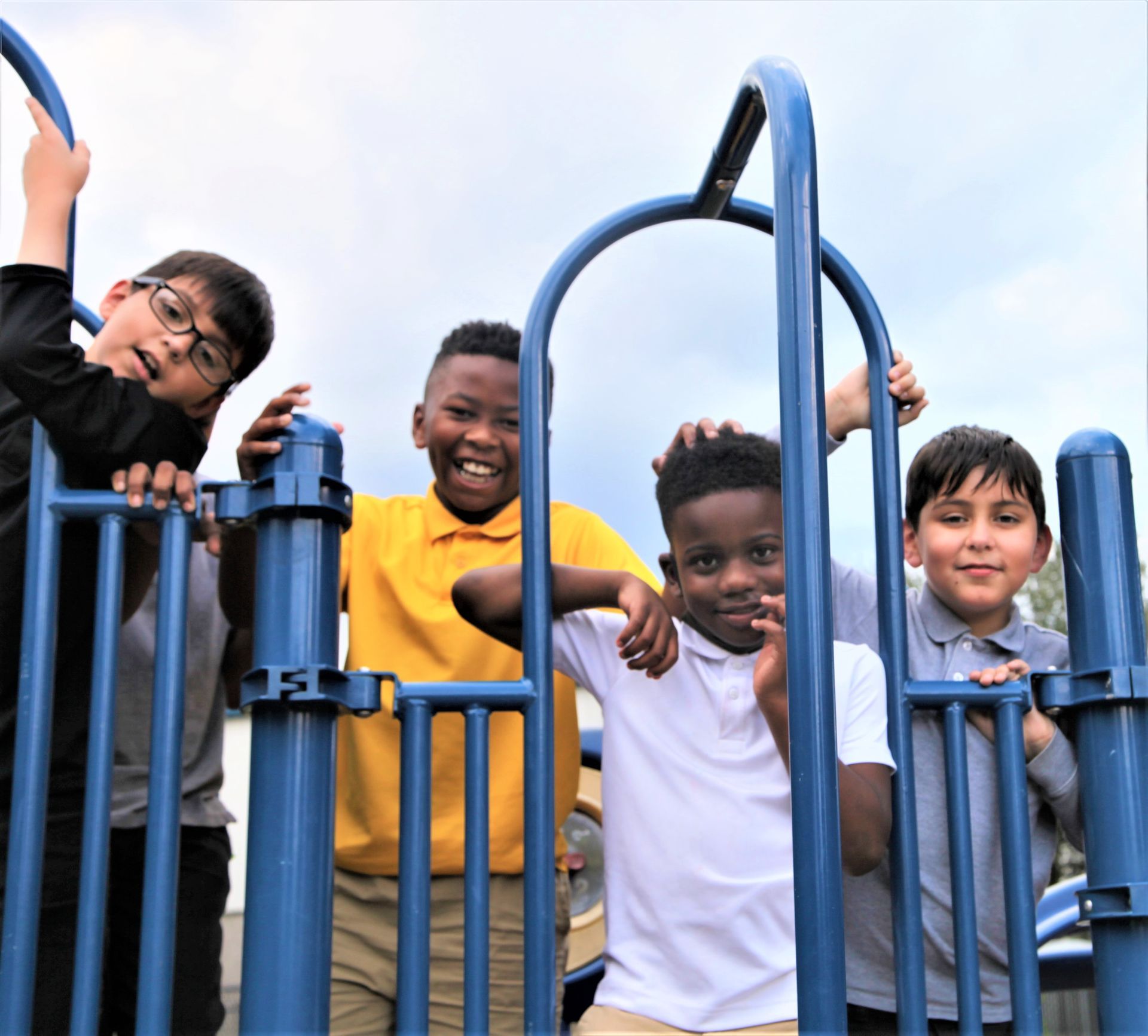 Group of smiling schoolboys on a blue playground structure, looking at the camera.