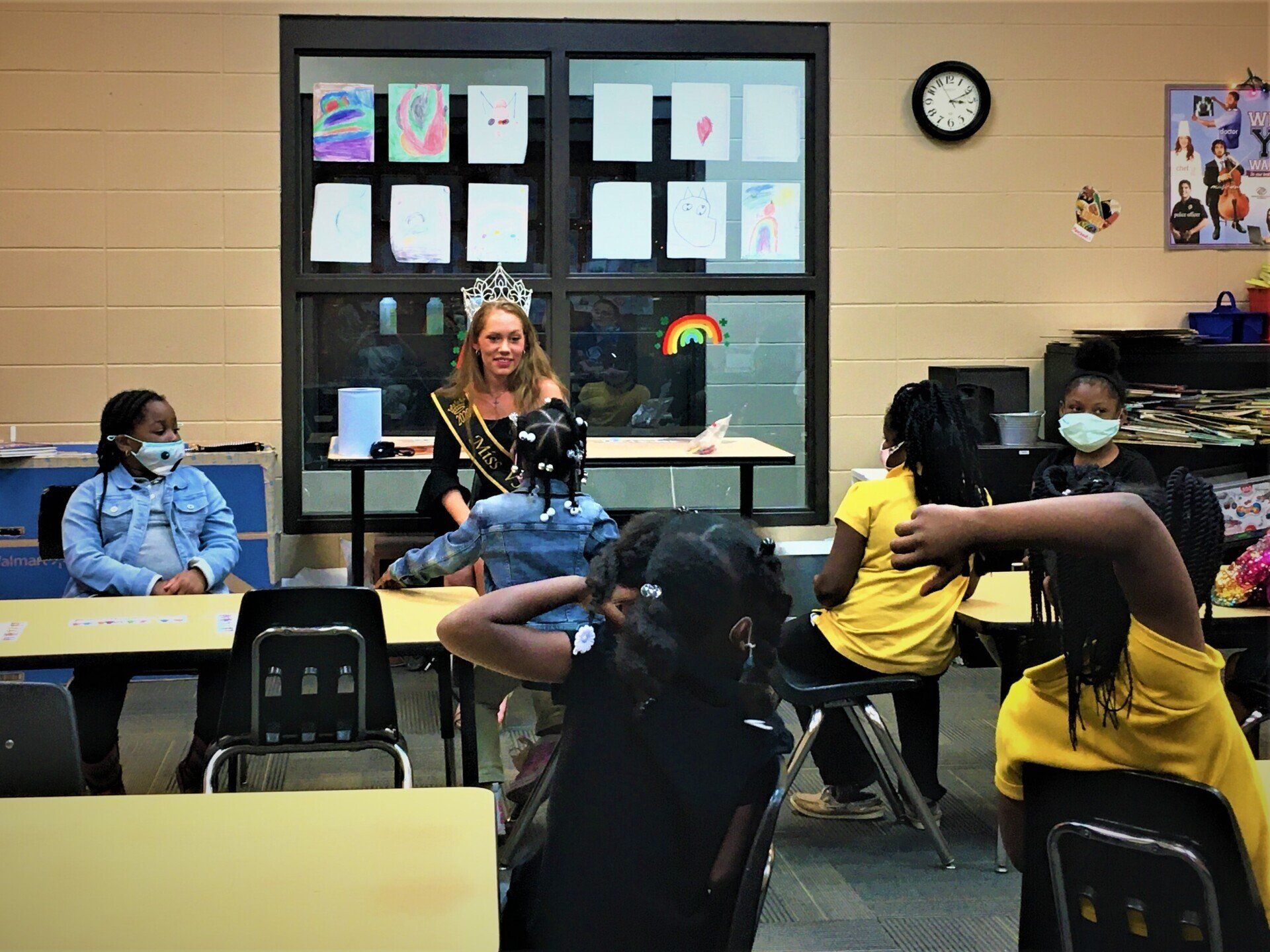 Beauty pageant winner sitting with students working on classroom activities at Boys & Girls Club