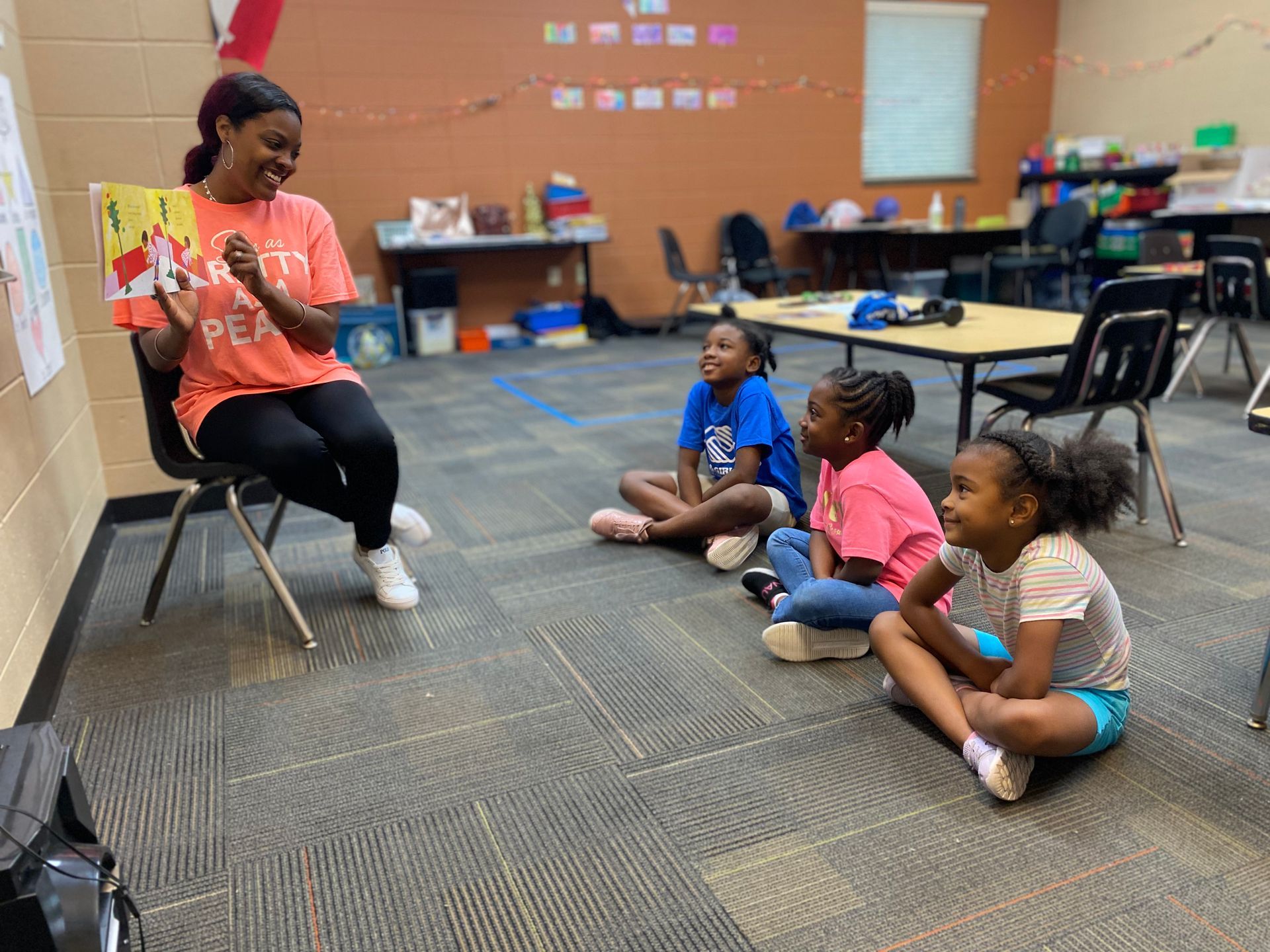 A woman reading to three young girls sitting on the floor in a classroom.