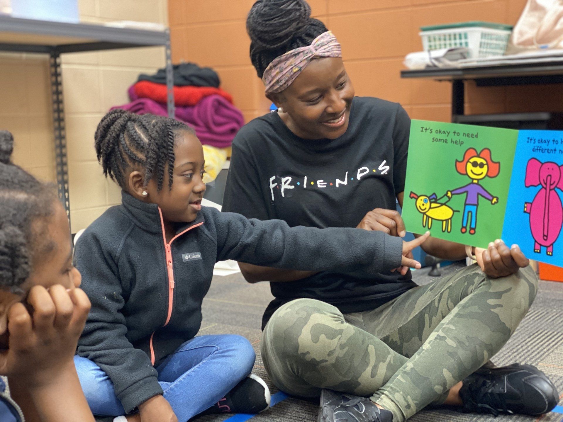Woman reading book to children, all sitting on floor; colorful illustrations, smiles.