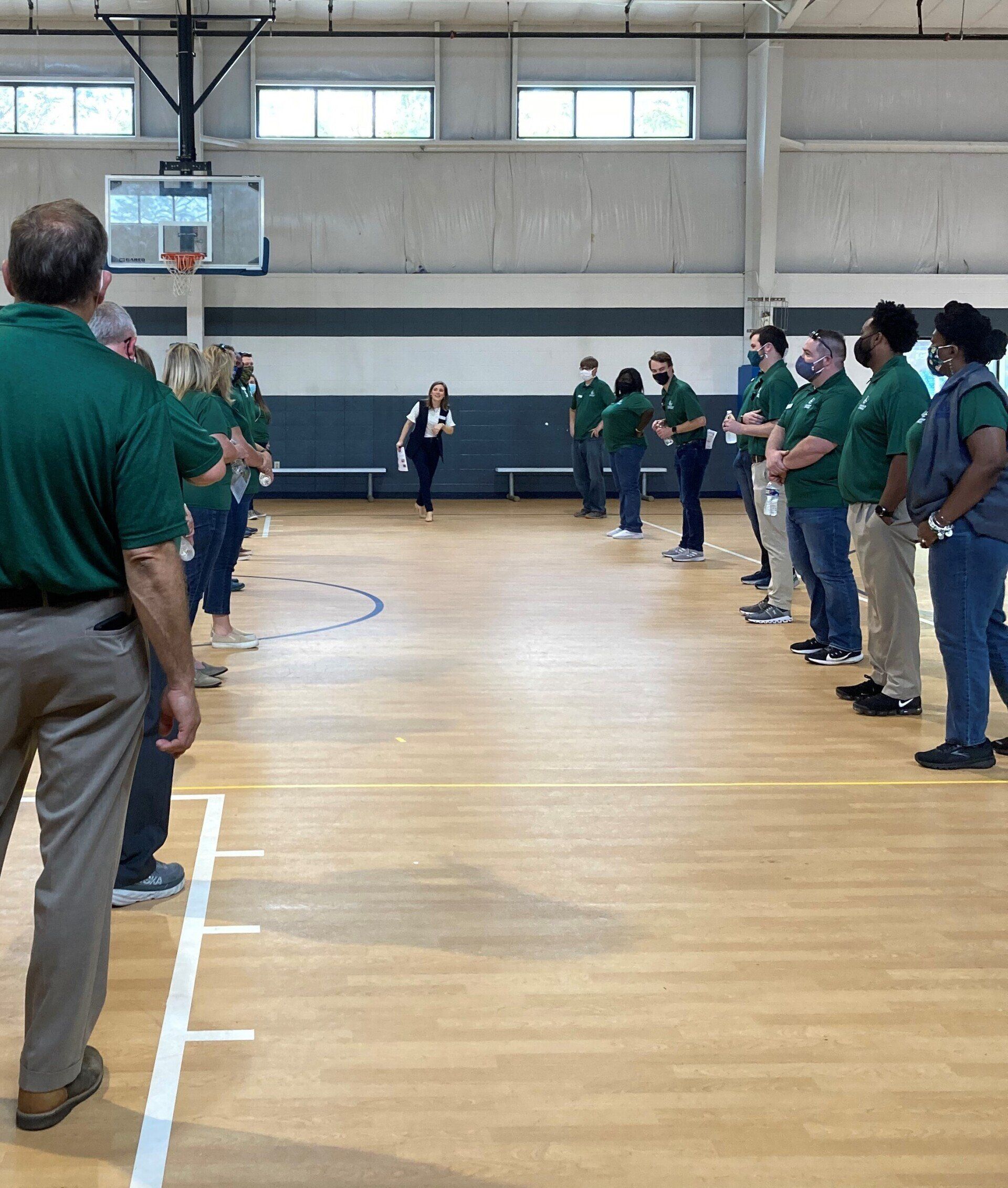 People in green shirts and masks standing in a gymnasium facing each other, some shaking hands.