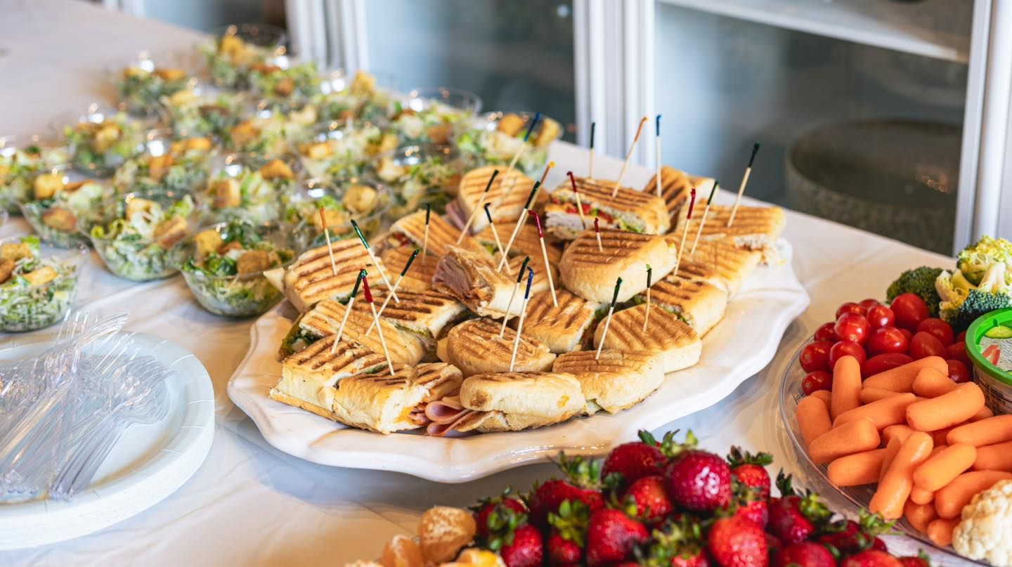 Buffet table with sandwiches, salads, fruits, and vegetables.