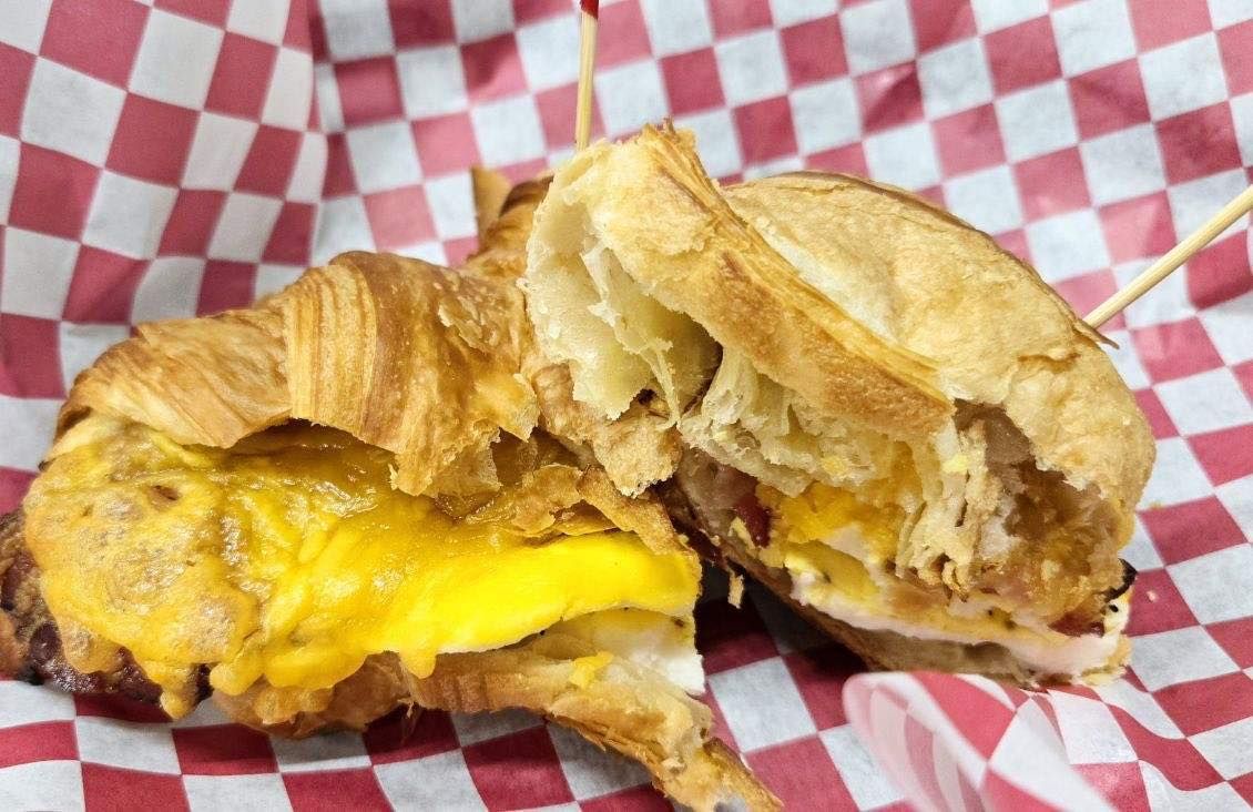 Croissant sandwich cut in half, with egg and cheese, served in red and white checkered paper.