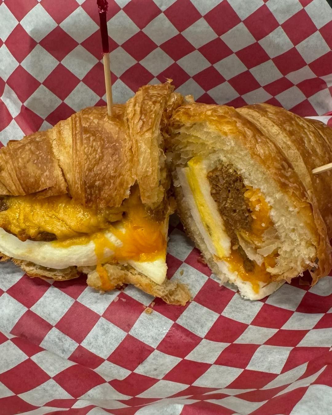Croissant sandwich cut in half, with egg, cheese, and filling, on red and white checkered paper.