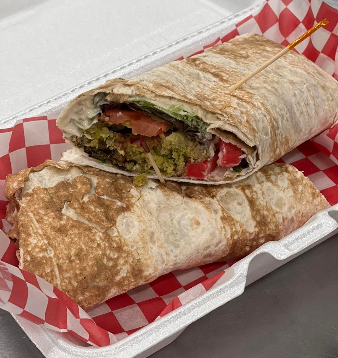 Falafel wrap cut in half, in a container with red and white checkered paper.