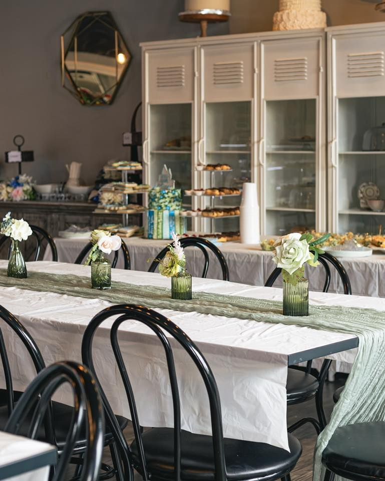 Long table set for an event with green runner, black chairs, white flowers, and display cases in the background.