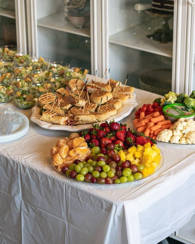 A buffet table with a variety of food: sandwiches, fruits, vegetables, and dip.