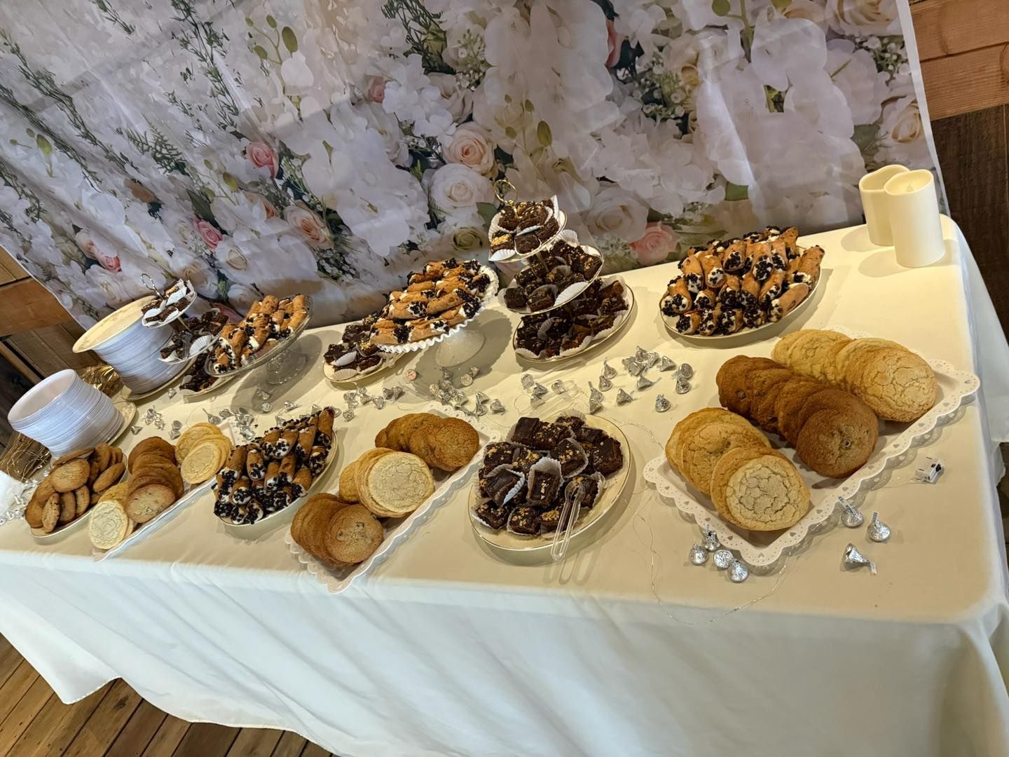 Dessert buffet with various pastries and cookies on a white tablecloth, decorated with silver accents.